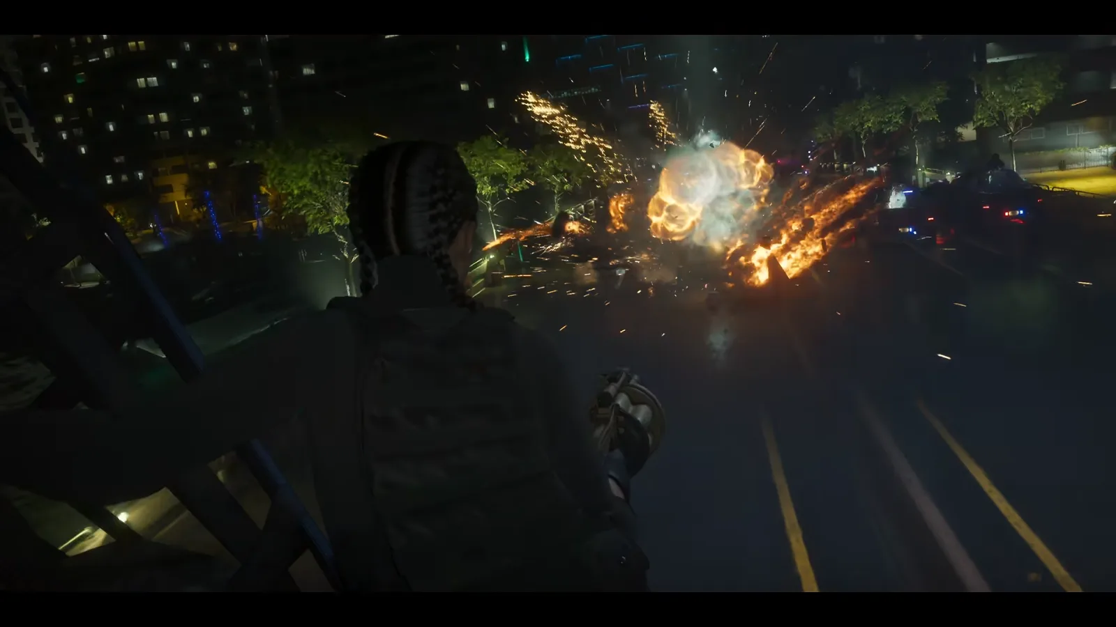 GTA 6 Launch Trailer: a person with braids and a tactical vest fires a drum-fed launcher down at police cars as an explosion lights the street