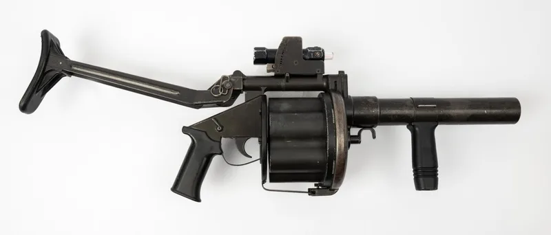 A real Milkor MGL 40mm six-shot grenade launcher made by Armscor, side view with the stock unfolded, museum photo on white