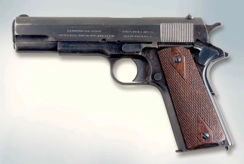 A real Colt M1911 .45 pistol with wooden grips, left side view, on a light grey background