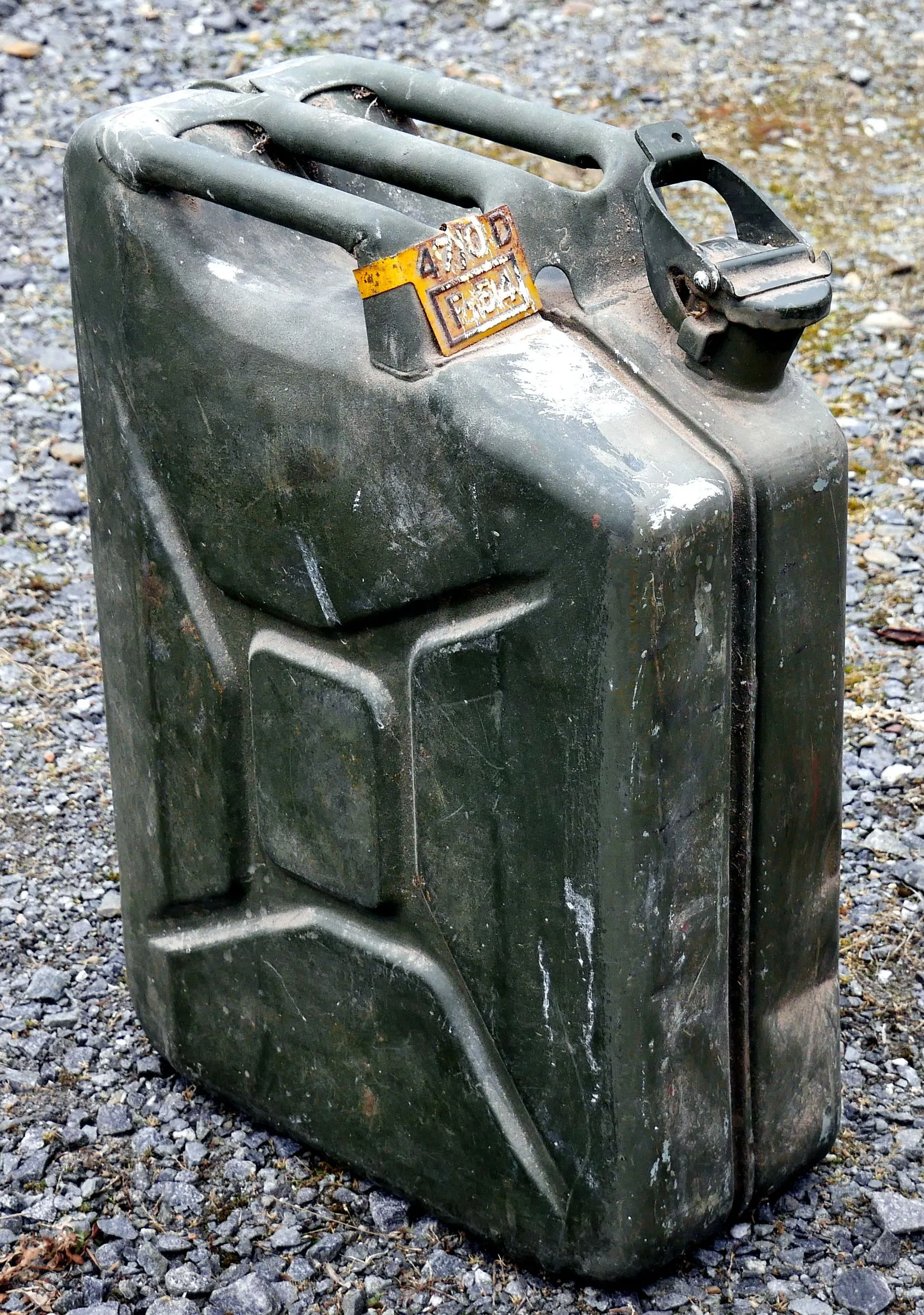 A real green steel 20-litre jerry can petrol canister, worn paint, standing on gravel