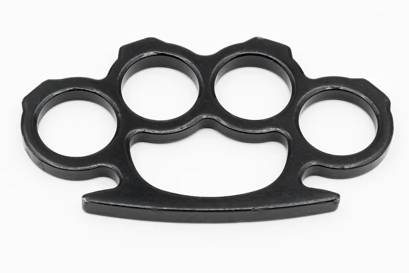 A real set of black metal brass knuckles with four finger rings, flat view on a plain white background