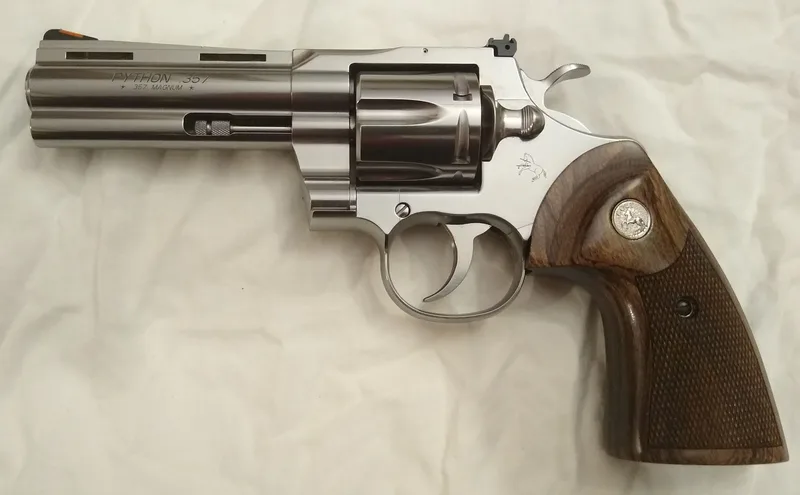A real 2020 Colt Python .357 Magnum revolver, stainless with a 4-inch barrel and walnut grips, side view on a white cloth