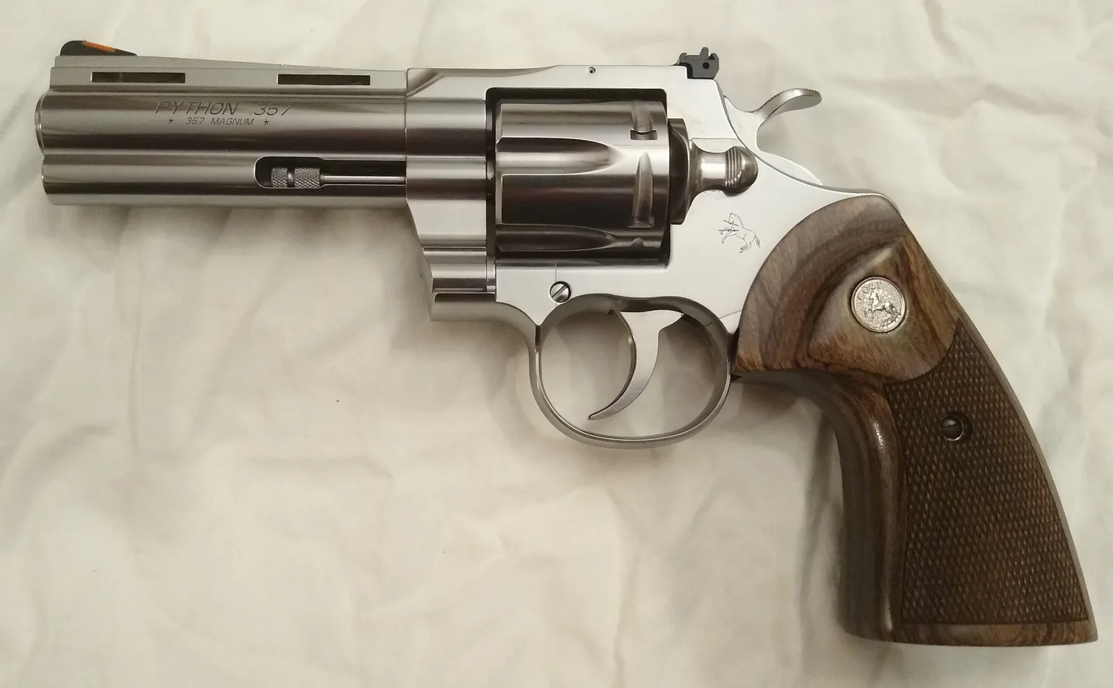 A real 2020 Colt Python .357 Magnum revolver, stainless with a 4-inch barrel and walnut grips, side view on a white cloth