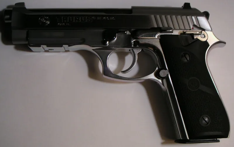 A real Taurus PT92 AFS 9mm pistol in stainless and black, right side view, on a light background