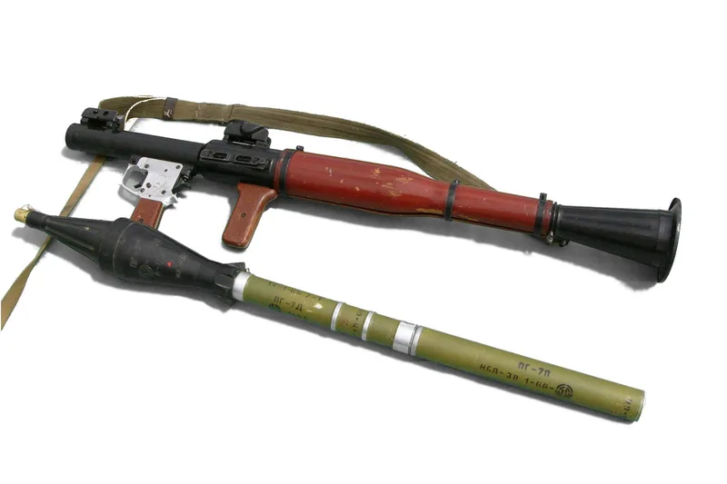 A real RPG-7 launcher with wooden heat guards and its rocket grenade lying beside it, on a white background