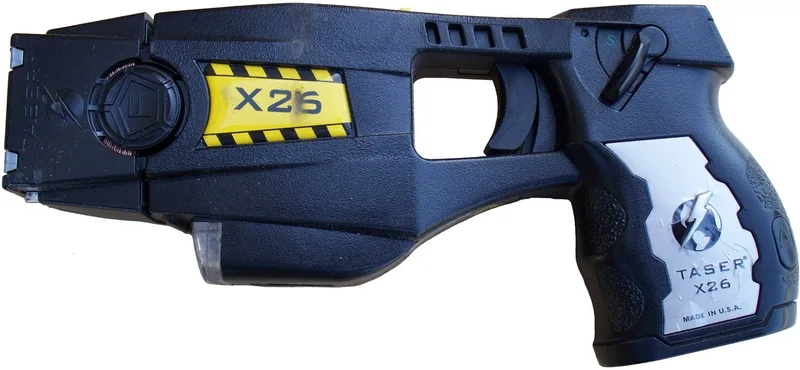 A real police-issue TASER X26 stun gun in black with a yellow X26 label, side view on a white background