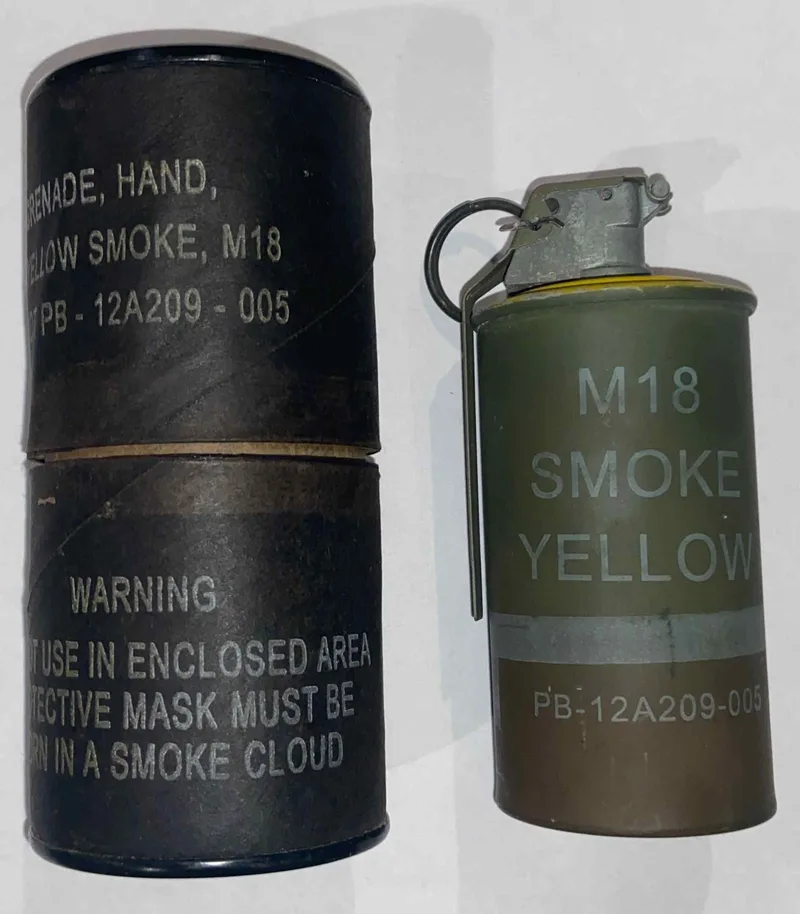 A real US M18 yellow smoke grenade next to its cardboard shipping tube, on a white background