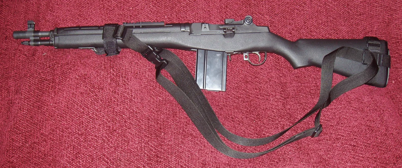 A real Springfield Armory M1A SOCOM 16 rifle with a black stock and sling, left side view, on a red cloth