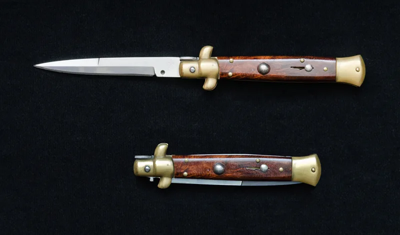 A real Italian stiletto switchblade with wooden scales and brass bolsters, shown open and closed on a black background