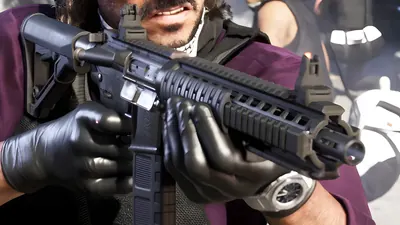 Close-up of a man in black gloves aiming a black AR-15-style carbine rifle, from an official GTA 6 screenshot