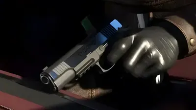 Close-up of a gloved hand holding a silver semi-automatic pistol in dim light, from an official GTA 6 screenshot