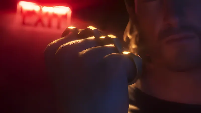 A clenched fist wearing gold knuckle dusters under a red exit sign, from the GTA 6 Launch Trailer