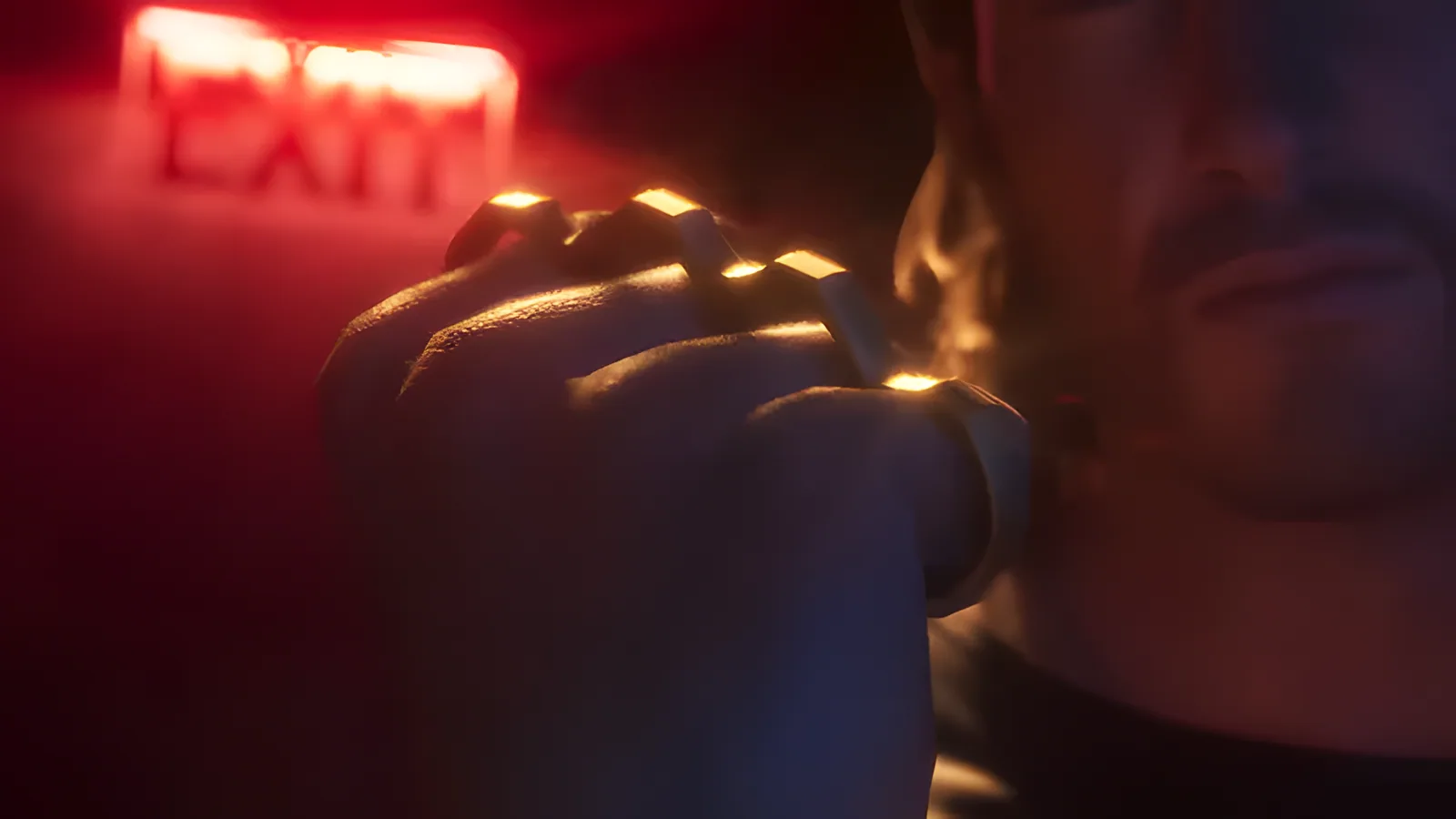 A clenched fist wearing gold knuckle dusters under a red exit sign, from the GTA 6 Launch Trailer